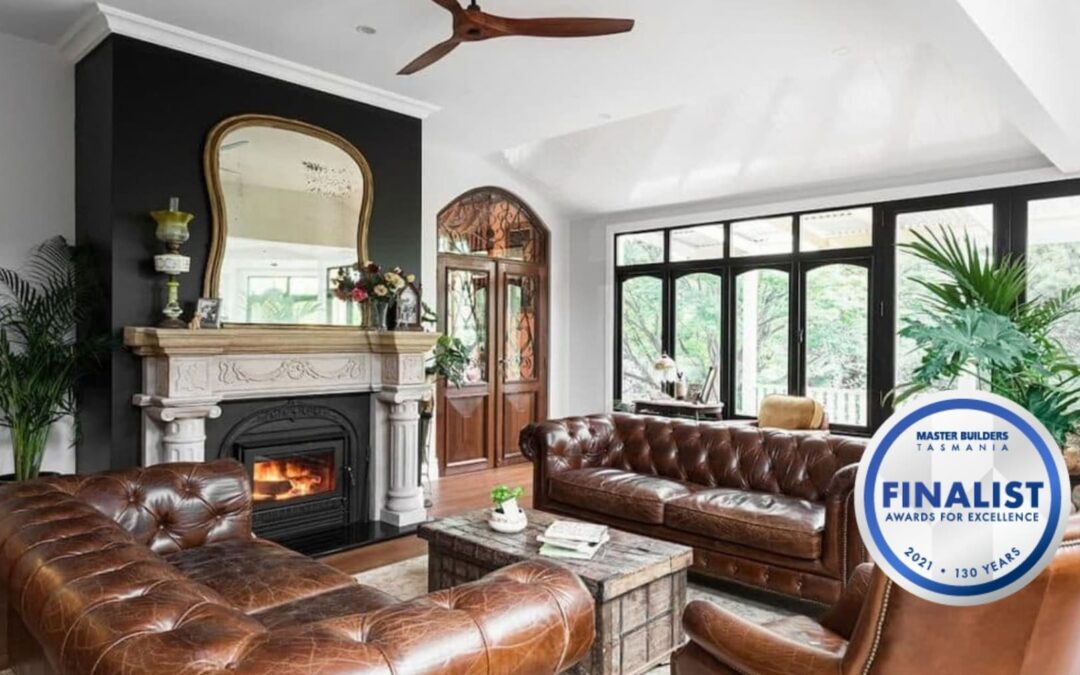 A living room with brown leather sofas, a fireplace, a large mirror, and tall windows showing greenery. A finalist award badge is in the corner.