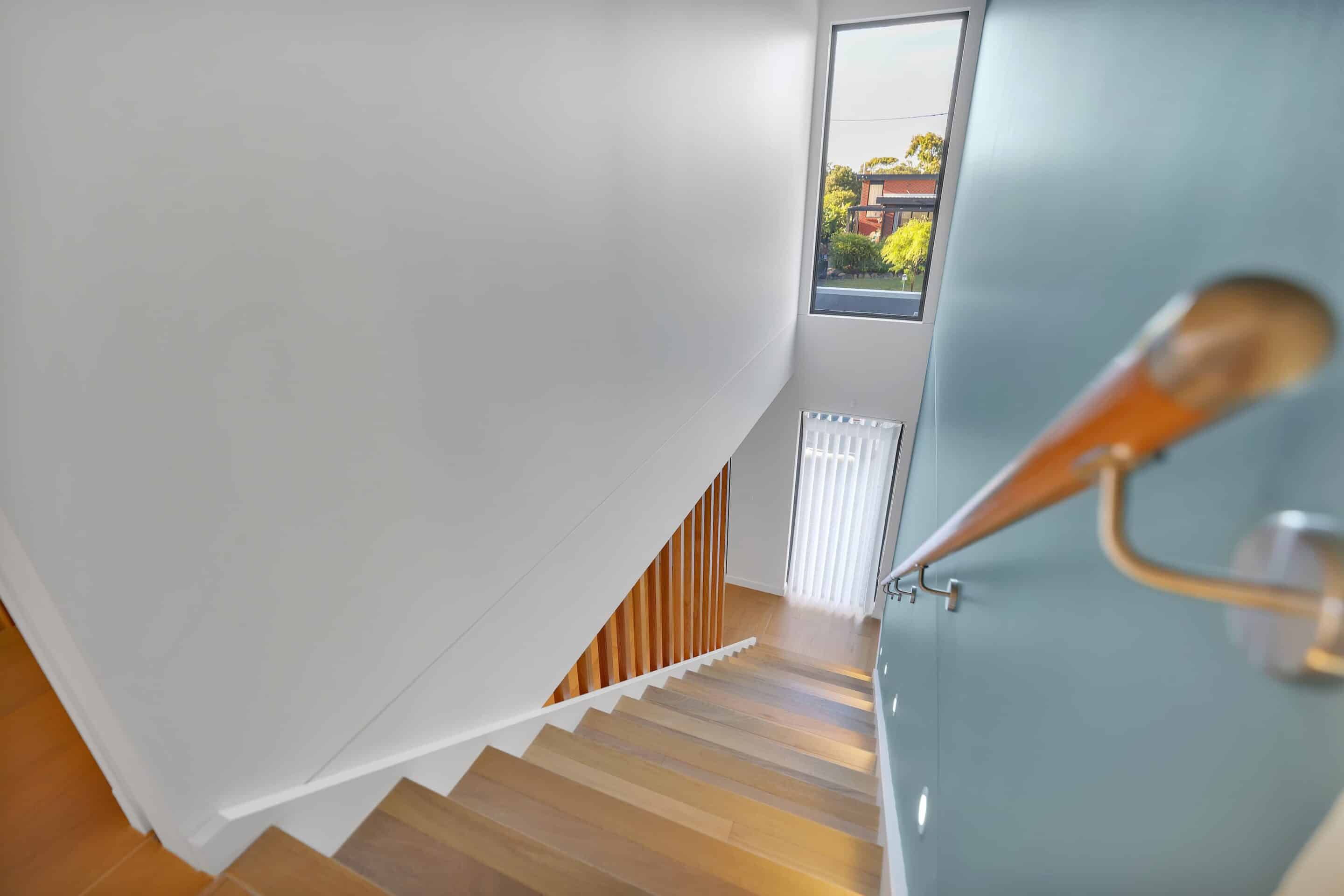 SC Turners Beach i-20 (1) View looking down a modern wooden staircase with a blue accent wall, handrail, vertical windows, and natural light coming in from outside.