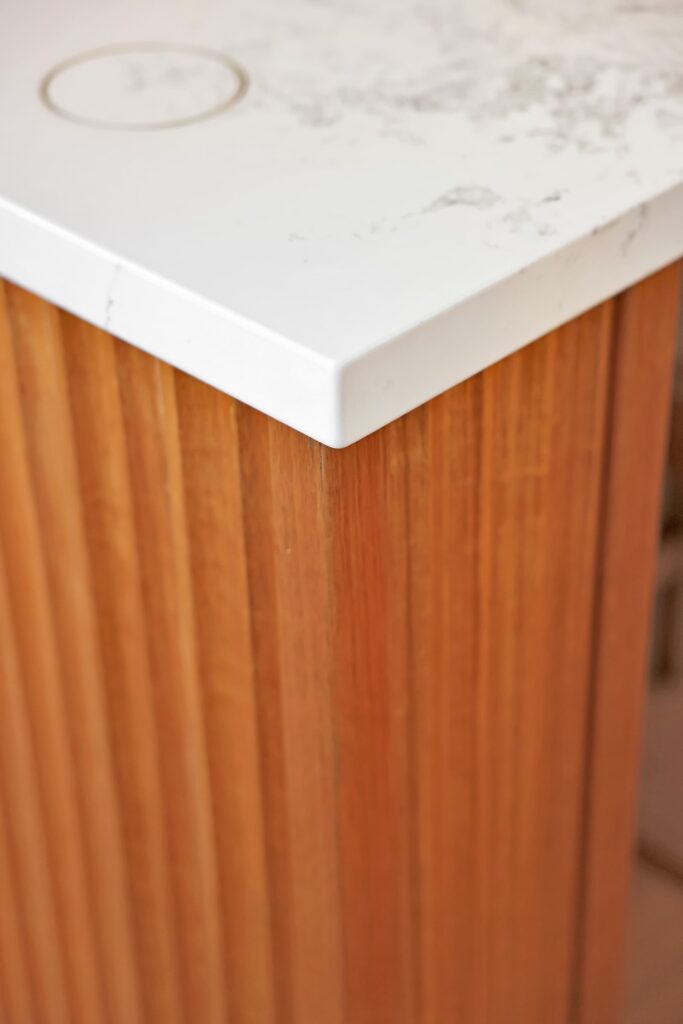 A close-up of a corner of a white marble countertop on a vertical wooden panel cabinet with a circular stain on the surface.