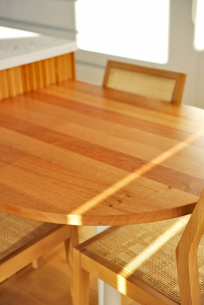 A wooden dining table with two matching chairs sits in sunlight, with shadows and light patterns visible on the surface.