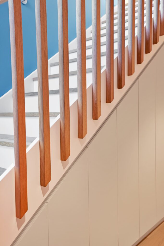 Close-up of wooden stair railing with vertical balusters and white paneling, set against a blue wall background.