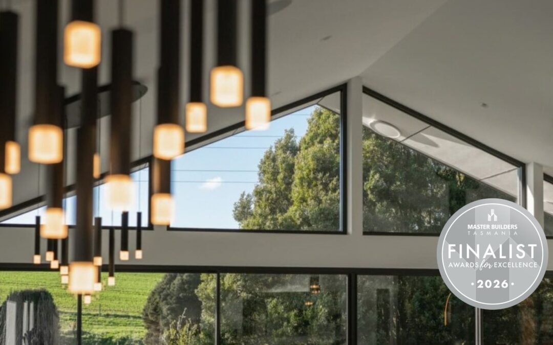 Modern interior with geometric windows, hanging pendant lights, and green trees visible outside. A circular badge on the right reads “Finalist Awards for Excellence 2026.”.